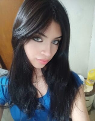 Portrait of a young woman with long dark hair and blue eyes looking at the camera, wearing a blue top.