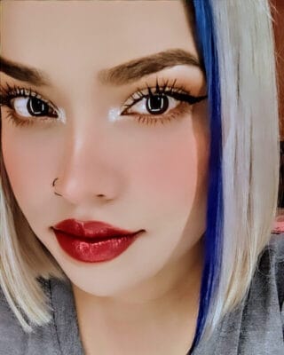 Close-up portrait of a woman with bold makeup: red lips, winged eyeliner, and a nose hoop, with blue and blonde hair.