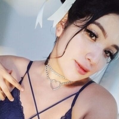 Close-up portrait of a smiling woman wearing a heart necklace and navy lace top with thin straps.